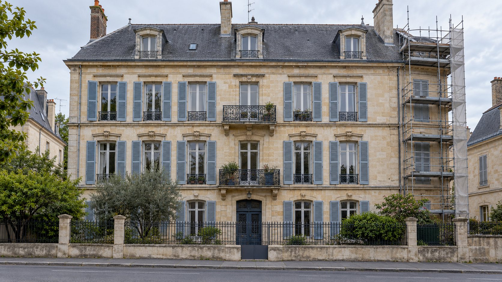 Façade en pierre d'un immeuble ancien avec des volets gris et un échafaudage sur un côté